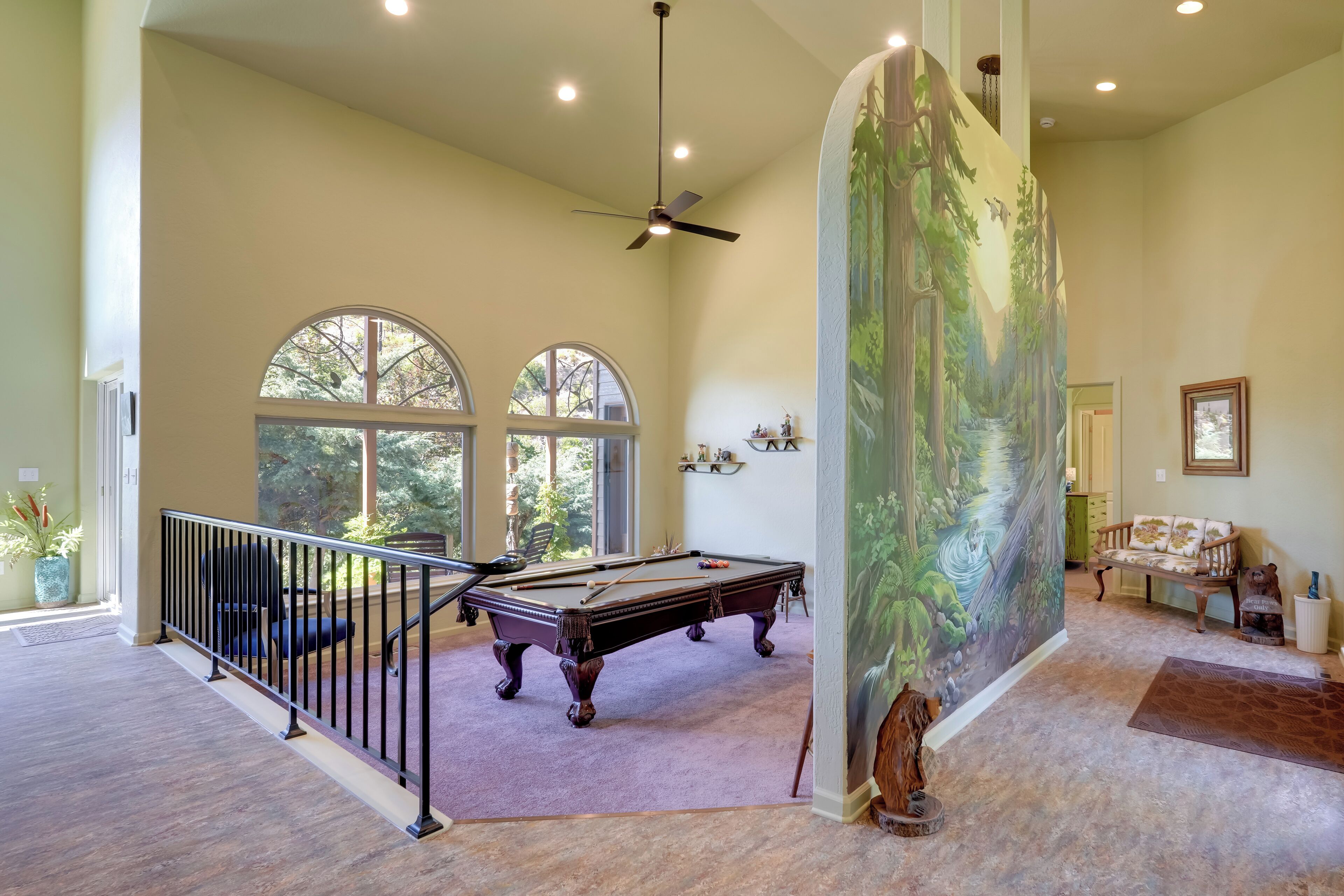 A spacious room with a pool table, a staircase with a railing, and a large mural on the wall.