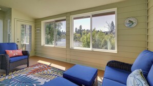 A sunroom with large windows, a blue sofa, a wicker chair, and a colorful rug. - On Mckenzie River! Home w/ Scenic Sunroom (Vida)
