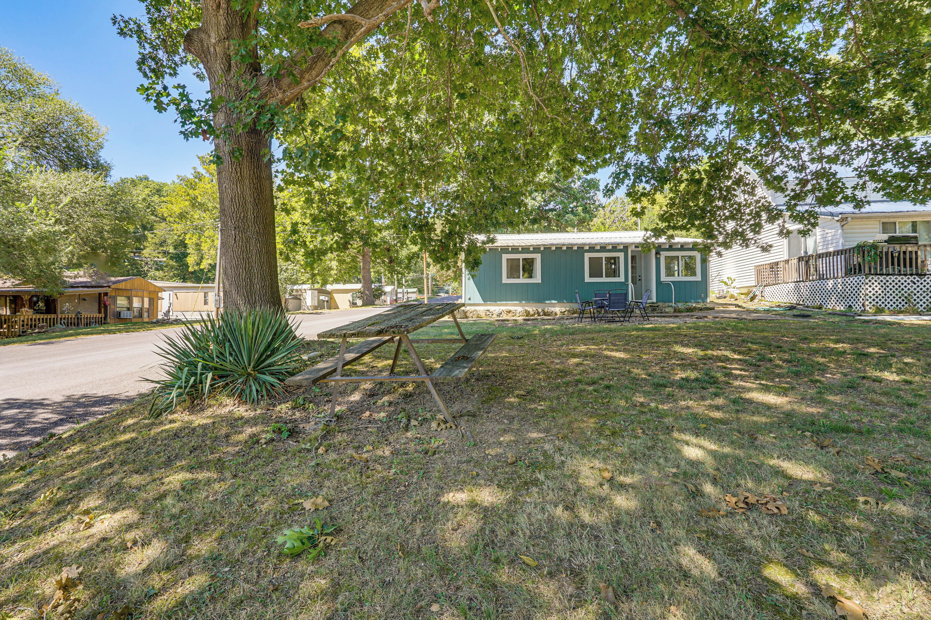 A small, single-story building with a blue exterior, a wooden deck, and a picnic table in a grassy yard.