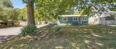 A small, single-story building with a blue exterior, a wooden deck, and a picnic table in a grassy yard.