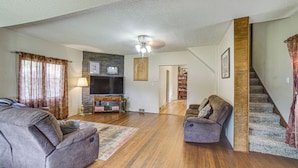 A spacious living room with hardwood flooring, a fireplace, a television, and a staircase leading to another level.
