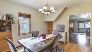 A dining area with a wooden table, chairs, a chandelier, and a view of the backyard through a window.
