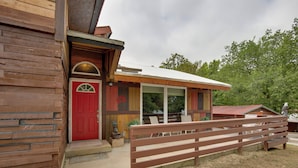 Un bâtiment rustique en bois, avec une porte rouge, un patio couvert et une clôture en bois.