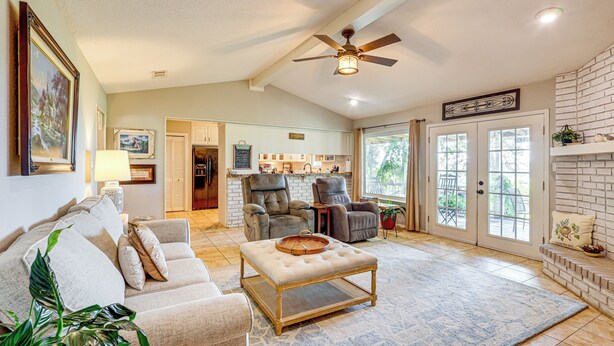 A spacious living room with a large window, a ceiling fan, and a dining area with a brick fireplace. - Boqsue River Valley Views! 3-acre Country Home (Valley Mills)