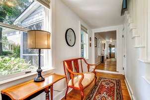 A hallway with a wooden desk, a chair, a rug, and a wall clock.