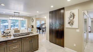 A modern kitchen with dark cabinetry, a marble countertop, and a piano in the background.