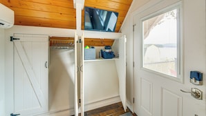 Een gang met een houten plafond, een deur met een raam en een plank met tassen.