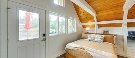 Un dormitorio con techo de madera, una cama con manta color crema y una ventana con persianas.