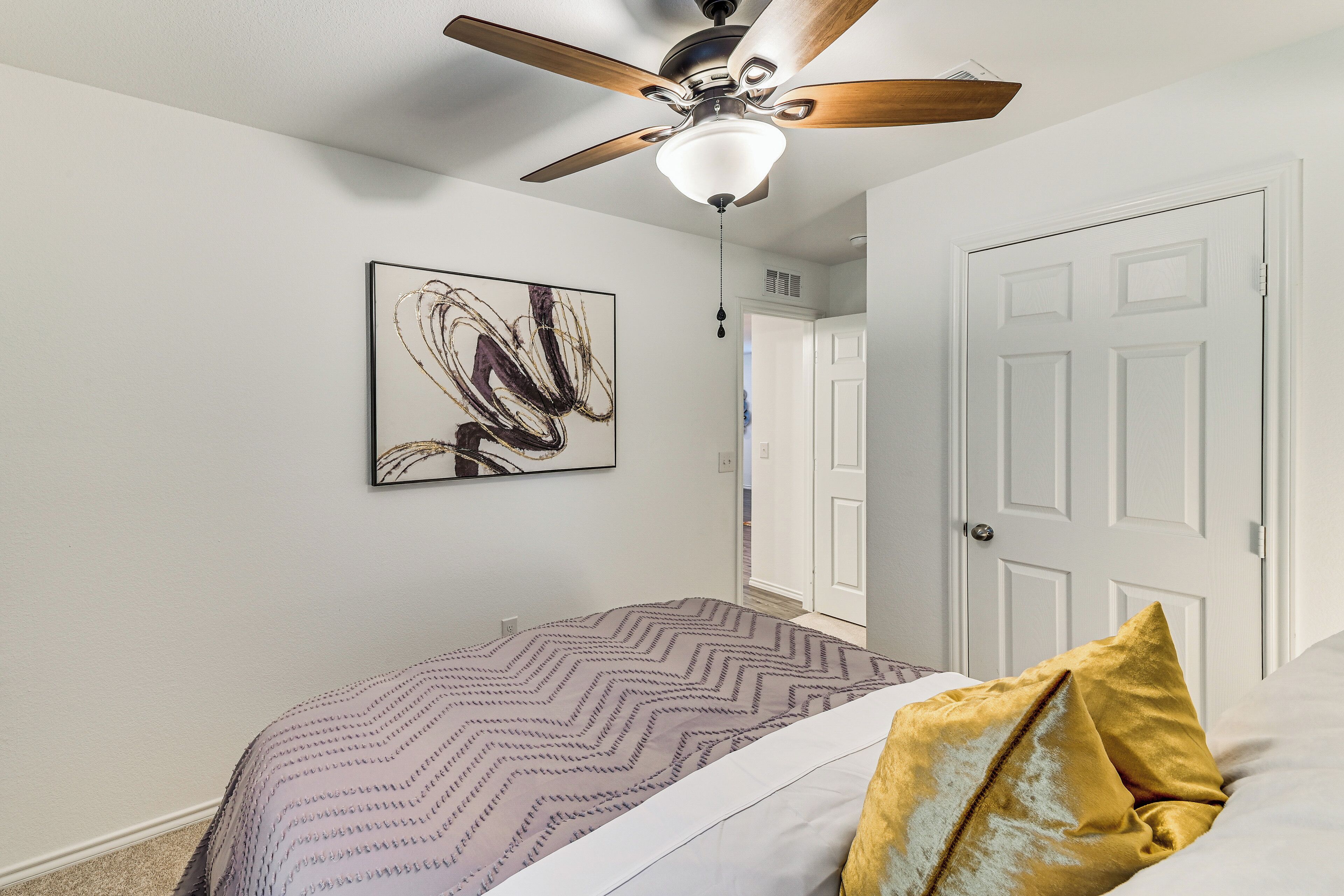 Une chambre à coucher avec un lit, un ventilateur de plafond, une porte et un tableau abstrait accroché au mur.