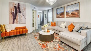 A modern living room with a sectional sofa, a round coffee table, and a chandelier. - Modern Comforts + Fenced Yard: Princeton Retreat! (Princeton)