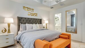 A bedroom with a tufted headboard, a large bed with an orange bench, a white nightstand with a gold lamp, and a large mirror on the wall. - Modern Comforts + Fenced Yard: Princeton Retreat! (Princeton)