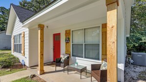 Een huis met een overdekte veranda, een rode deur en een klein terras met rieten meubels.