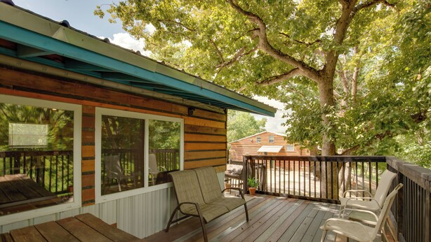 Une terrasse en bois avec un espace salon couvert, une table et un pot de fleurs.