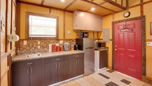 Une cuisine avec des meubles de rangement en bois foncé, un réfrigérateur en acier inoxydable, un four à micro-ondes et une porte rouge.