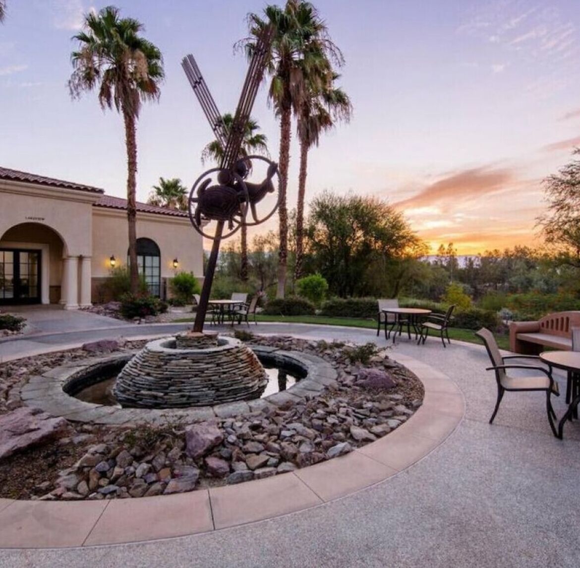A courtyard with a stone fountain, palm trees, and outdoor seating.
