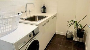 A compact laundry room with a washing machine, a sink, and a small window.
