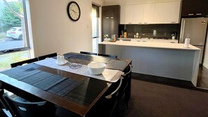 A modern kitchen with white cabinets, a black refrigerator, and a dining area with a wooden table and chairs.