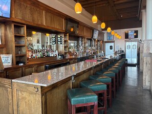 A bar area with a long counter, multiple shelves with bottles, and green bar stools.