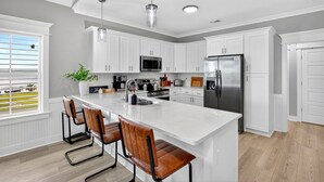 A modern kitchen with white cabinetry, stainless steel appliances, and a large island with bar stools. - Tranquil Waterfront Retreat: Stunning Bay Views Near Downtown Bay St. Louis (Bay St. Louis)