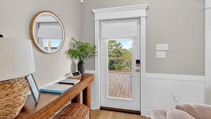 A room with a wooden desk, a mirror, a potted plant, a white door leading to a balcony, and a view of greenery outside. - Tranquil Waterfront Retreat: Stunning Bay Views Near Downtown Bay St. Louis (Bay St. Louis)
