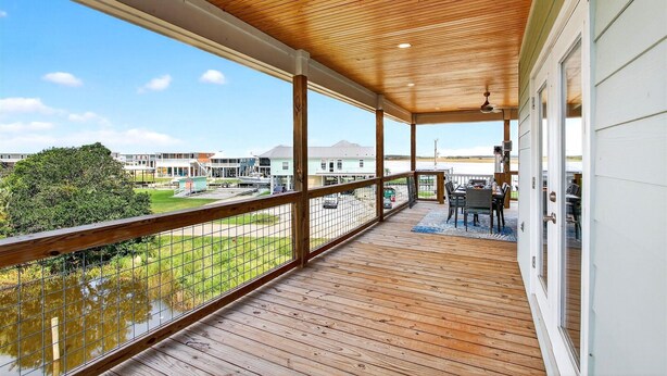 A covered balcony with a wooden floor and railing, overlooking a grassy area and buildings. - Tranquil Waterfront Retreat: Stunning Bay Views Near Downtown Bay St. Louis (Bay St. Louis)
