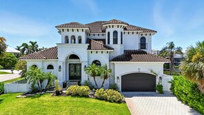 Une grande maison blanche à plusieurs étages, avec un toit en tuiles, de nombreuses arcades et un garage.