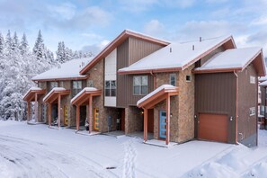 Ein mehrstöckiges Gebäude mit einer Stein-Fassade und Holzelementen, das mehrere Eingangstüren und eine schneebedeckte Landschaft aufweist.