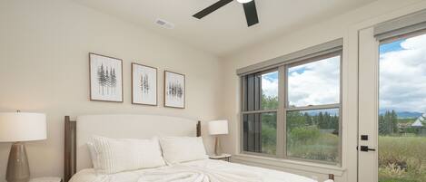 A bedroom with a large bed, two bedside tables with lamps, a ceiling fan, and a window with a view of greenery and mountains.
