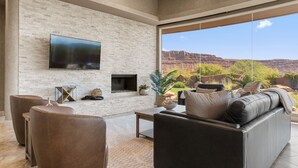 A modern living room with a fireplace, leather sofas, and a large TV mounted on a brick wall.