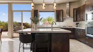 A modern kitchen with a large island, dark wood cabinets, stainless steel appliances, and a view of the outdoors.