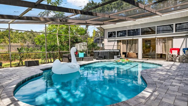 A swimming pool with a swan float, surrounded by a covered patio area with a view of a modern house.