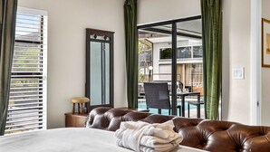 A hotel room with a bed, a chair, a table, and a view of a pool and balcony.