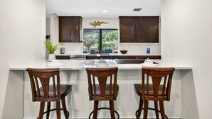 A kitchen with a large island, dark wooden cabinets, and a window with a view of greenery.
