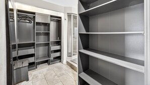 A walk-in closet with multiple shelves and hanging space, a glass door entrance, and a tiled floor.