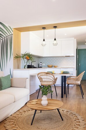 Een moderne keuken met witte kastjes, een houten aanrechtblad en een eethoek met rieten stoelen.