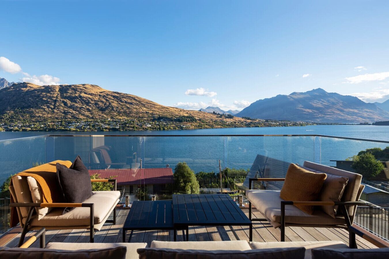A balcony with outdoor furniture, a glass barrier, and a view of a lake and mountains.