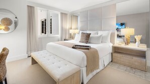 Una camera d'albergo moderna con un letto grande, una panca, un comodino con lampade e uno specchio.