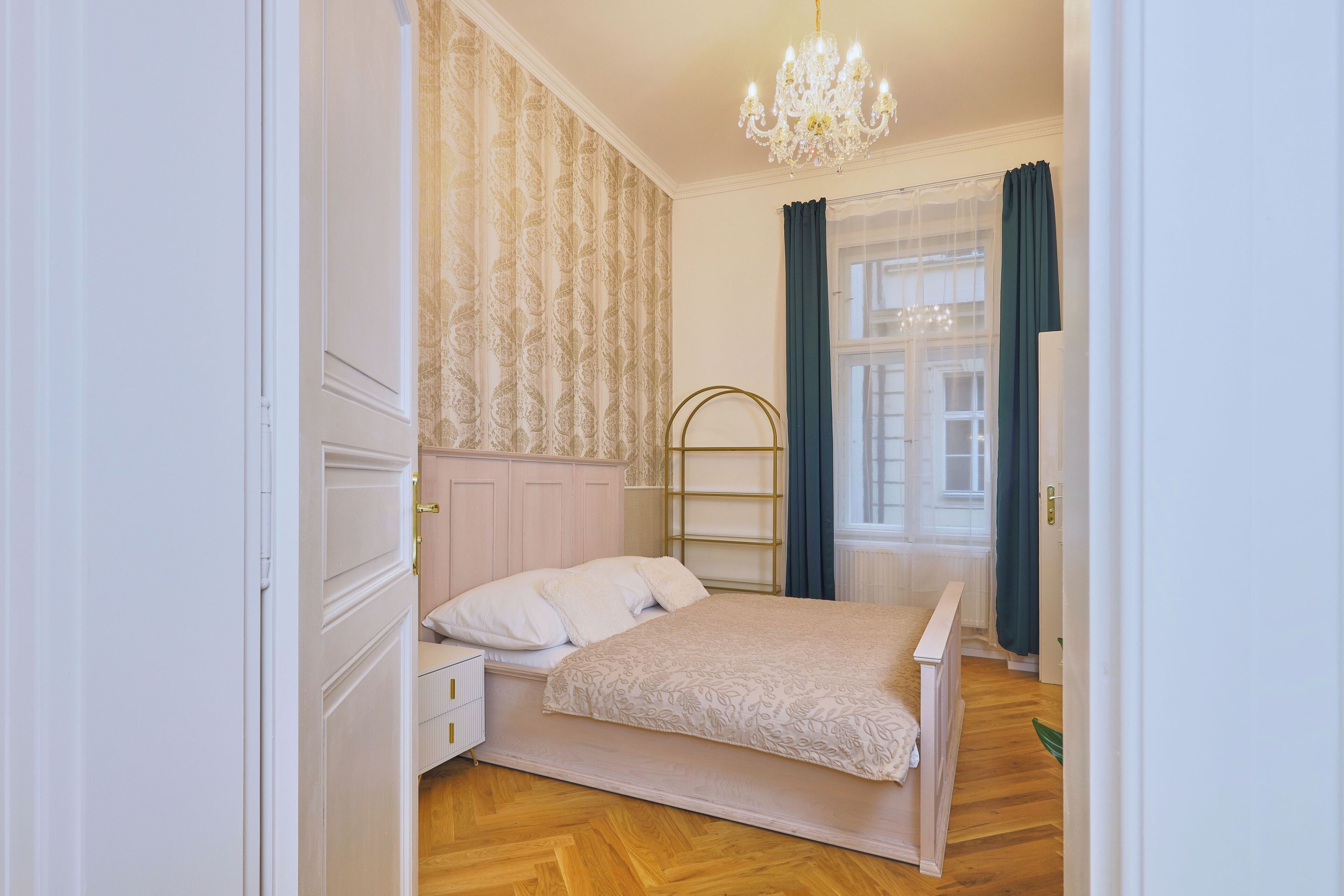 A bedroom with a bed, a nightstand, a dresser, a chandelier, and a window with curtains.