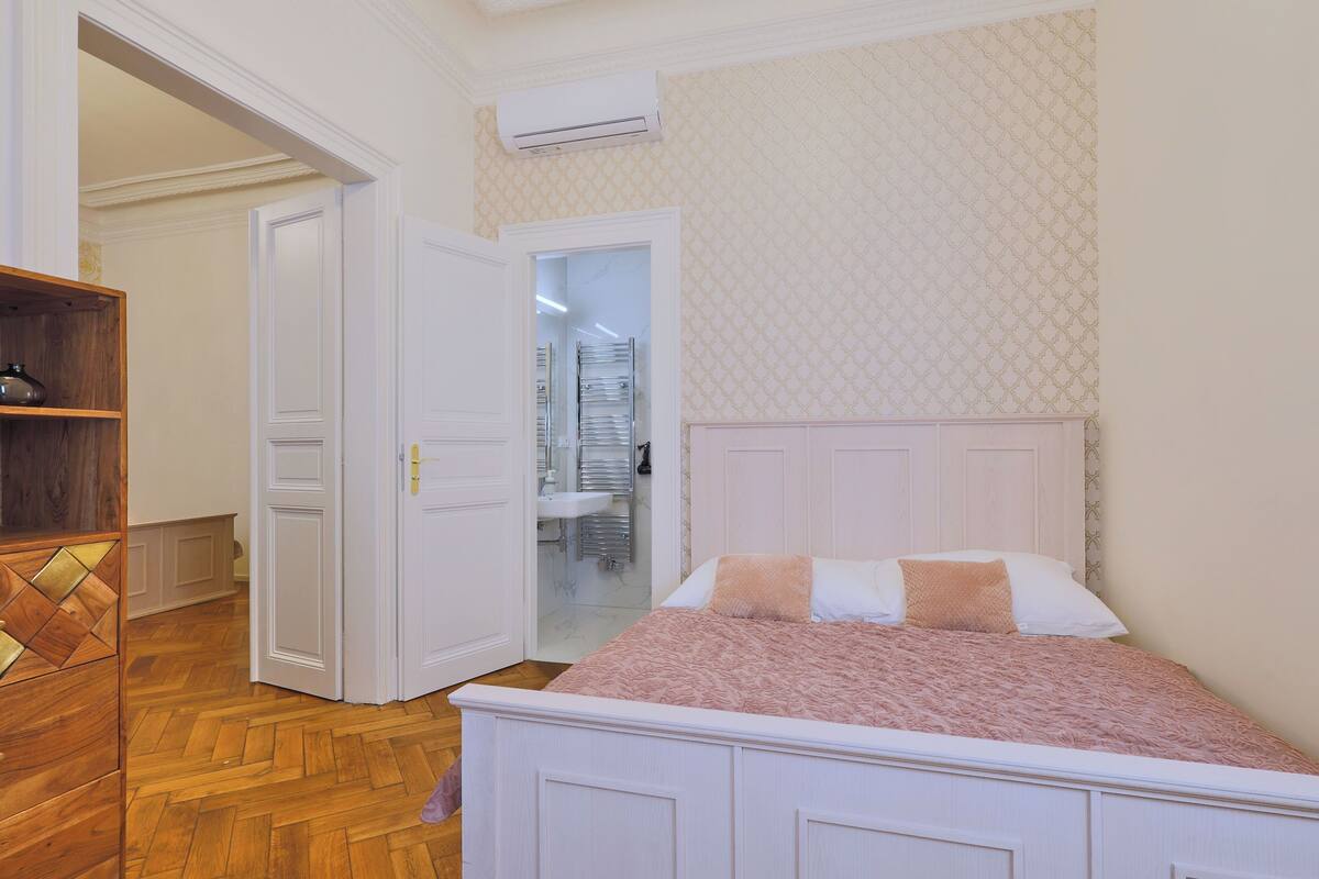 Een slaapkamer met een bed, een houten kast, een witte deur en een badkamer die door een open deur zichtbaar is.