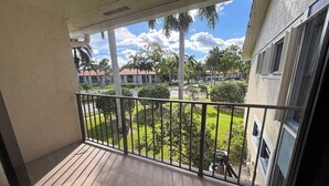 Ein Balkon mit Blick auf einen gepflegten Rasen, Palmen und ein Gebäude im Hintergrund.