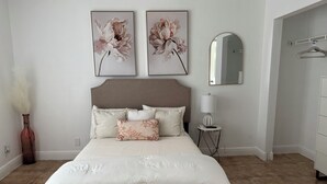 Ein ordentlich eingerichtetes Schlafzimmer mit einem großen Bett, einem Nachttisch mit Lampe und zwei gerahmten floralen Bildern an der Wand.