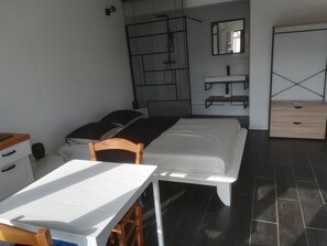 A modern bedroom with a bed, bedside table, chair, and a desk with a chair. There is a mirror, a shelf, and a wardrobe.