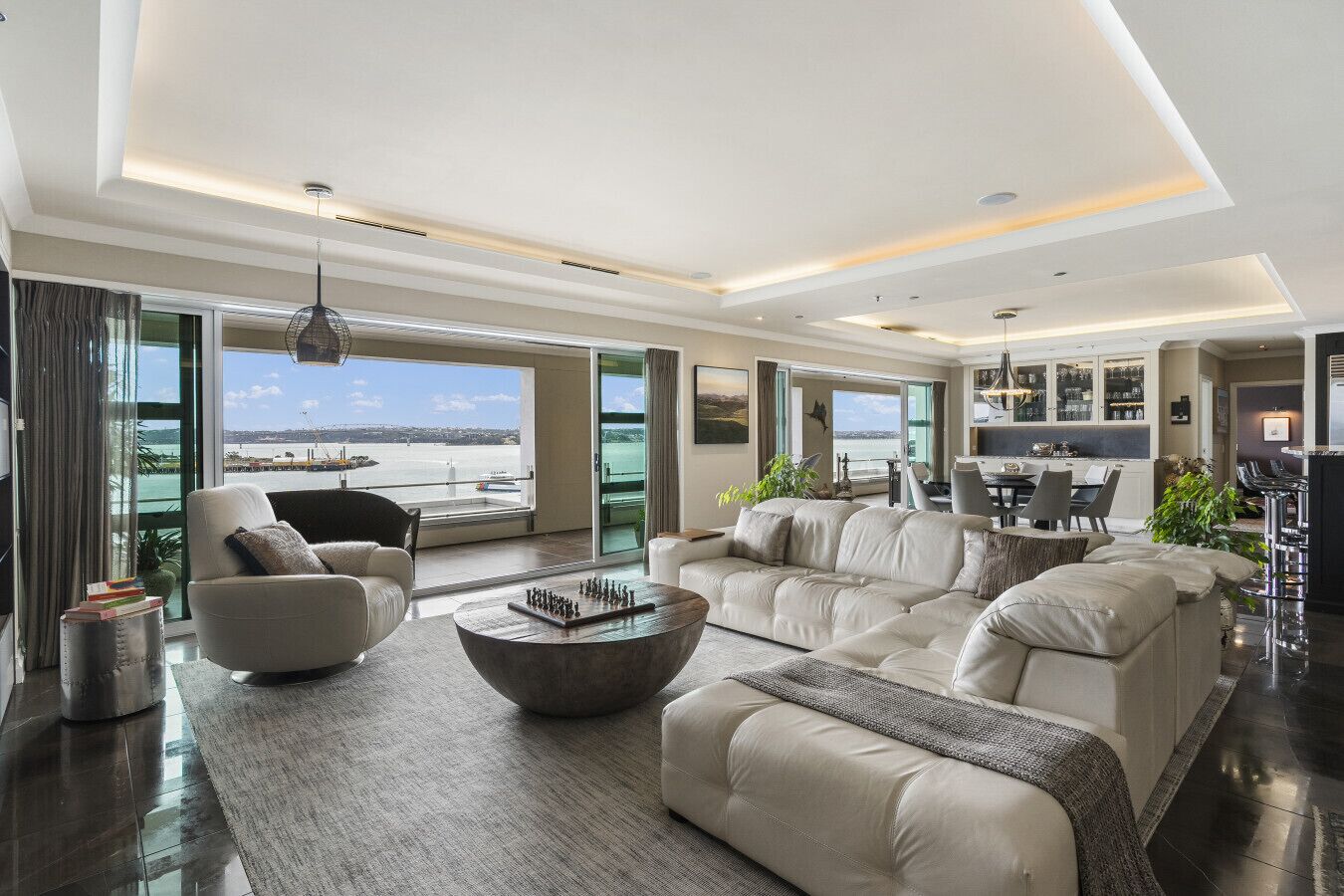 A spacious living room with a large sofa, a coffee table, and a view of a body of water through large windows.