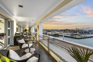 Een balkon met rieten stoelen en een tafel, met uitzicht op een jachthaven met boten en gebouwen.