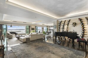 A spacious living room with a grand piano, a large rug, and a wall of wine bottles.