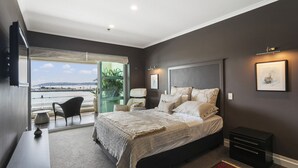 Un dormitorio moderno con una cama grande, un escritorio y una silla. Hay un balcón con vistas al mar.