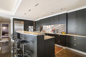 A modern kitchen with dark cabinetry, a marble backsplash, and a central island with bar stools.