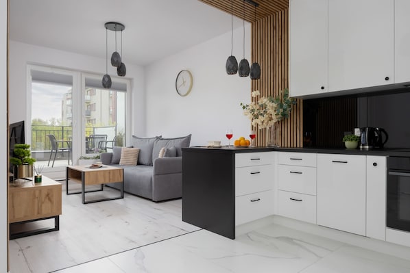 A modern kitchen with white cabinets, a black countertop, and a dining area with a grey sofa and coffee table.