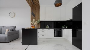 Eine moderne Küche mit weißen Schränken, einer schwarzen Arbeitsplatte und einem grauen Sofa im Wohnbereich.