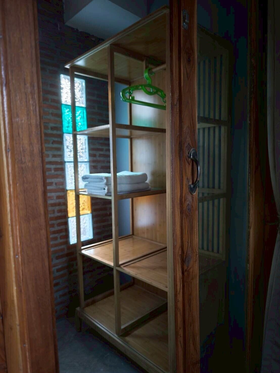 Un armario de madera con varios estantes, un perchero verde y una ventana con vidrio emplomado.